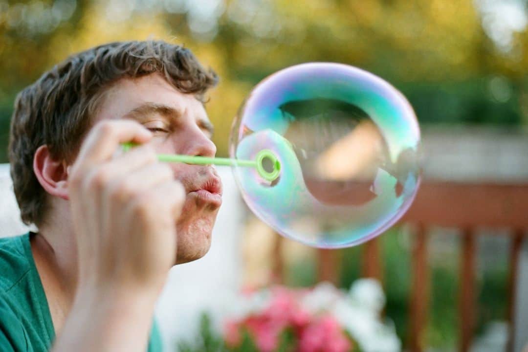 man blowing a soap bubble with bokeh in the background