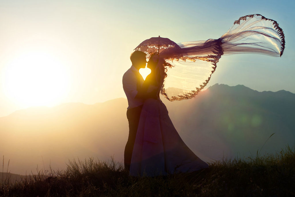 groom and bride kissing eachother at sunset over a decline